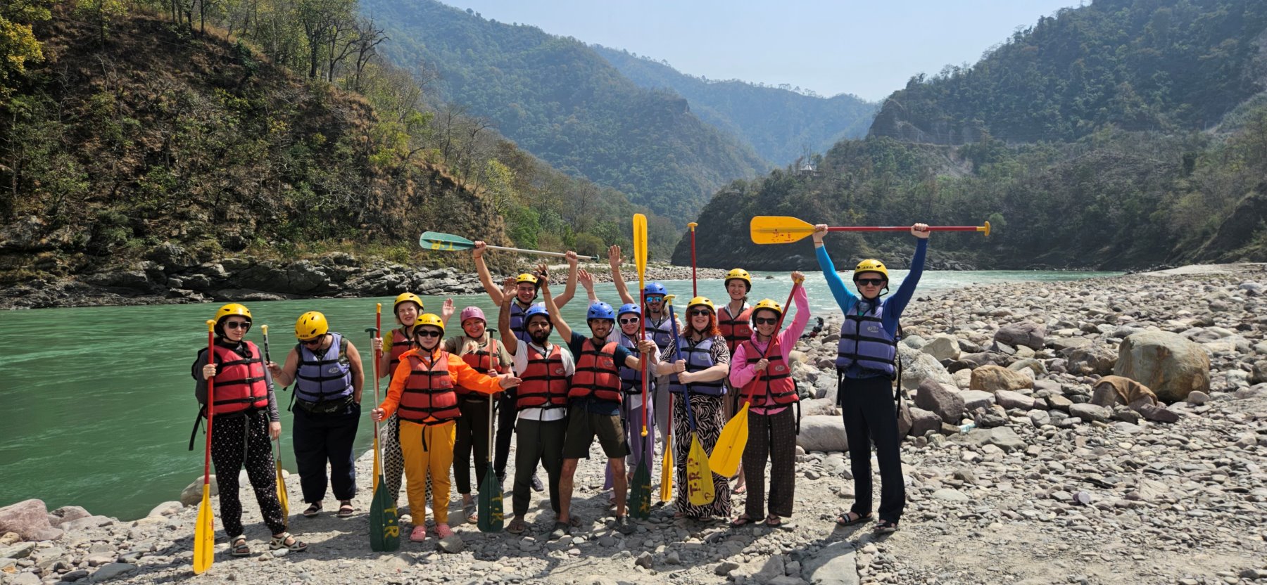 The group after a white-water rafting run on the Ganga, paddles raised, gorge walls on both sides