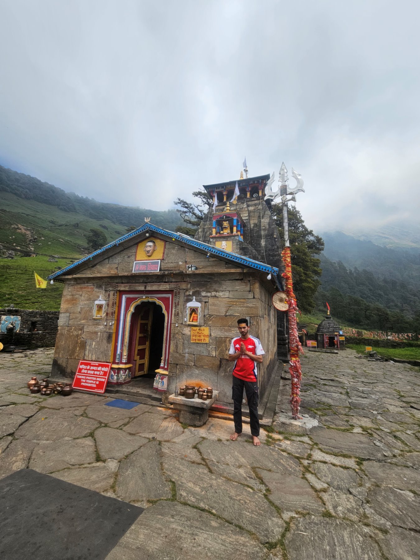 A guest standing in prayer outside the Tungnath temple, mist rolling down the hillside behind