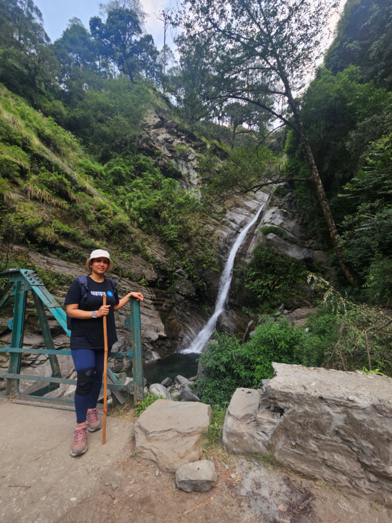 A guest resting on a trail bridge beside a waterfall in the forest