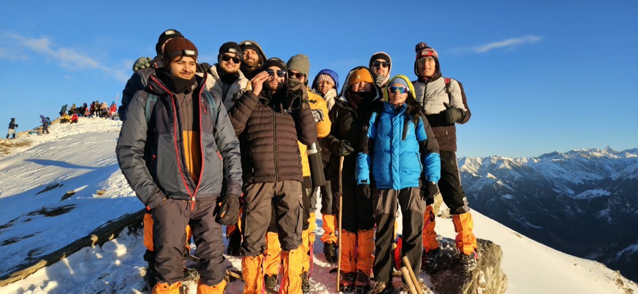 The trekking group gathered on a snowy summit ridge at sunrise, the Himalayan range spread out behind them