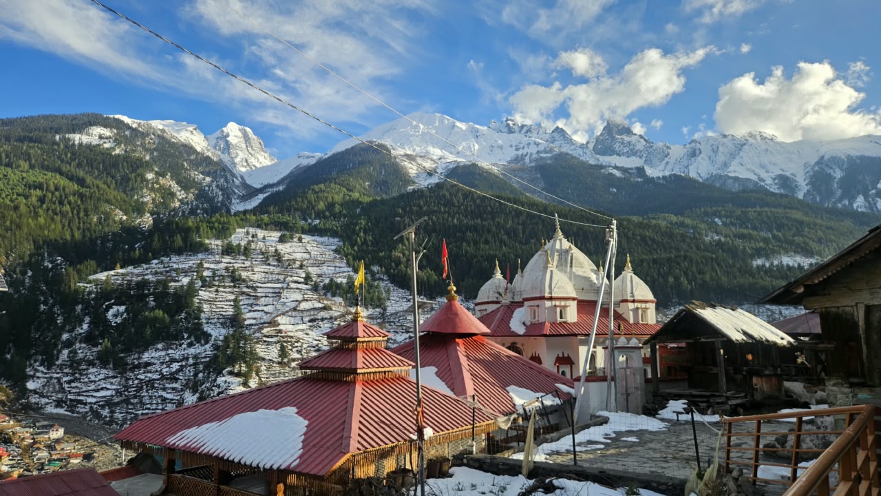 A red-roofed Himalayan temple complex set against snow-capped peaks
