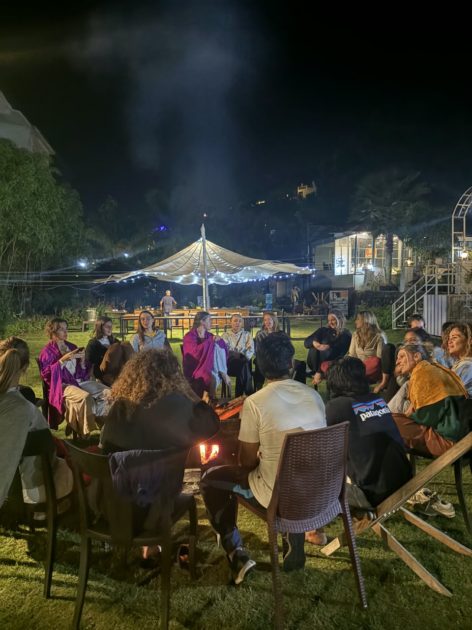 The group gathered by the fire under a lit tent at night