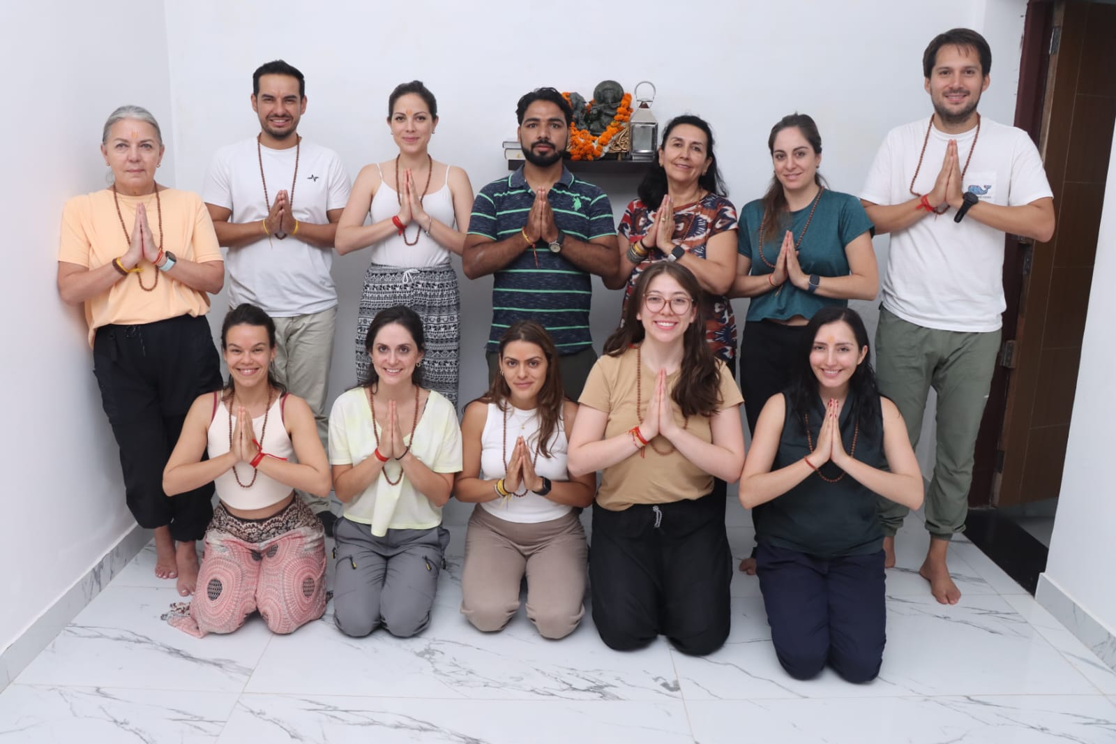 The group posing together indoors with palms joined in namaste