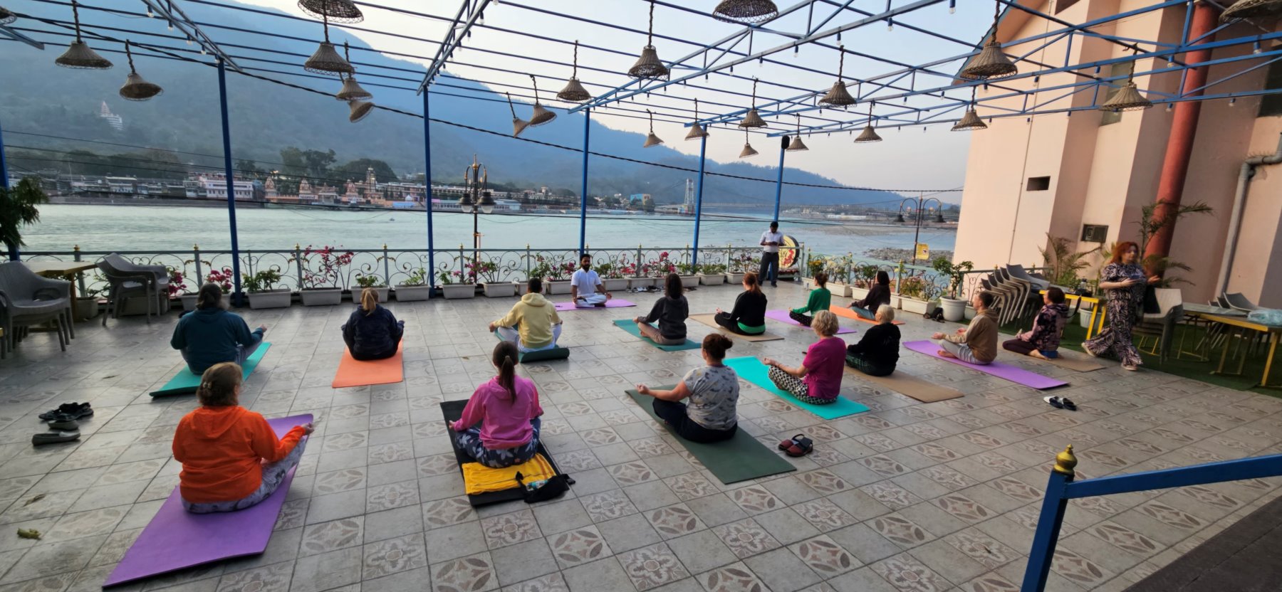Group yoga practice on a rooftop terrace above the Ganga at dusk