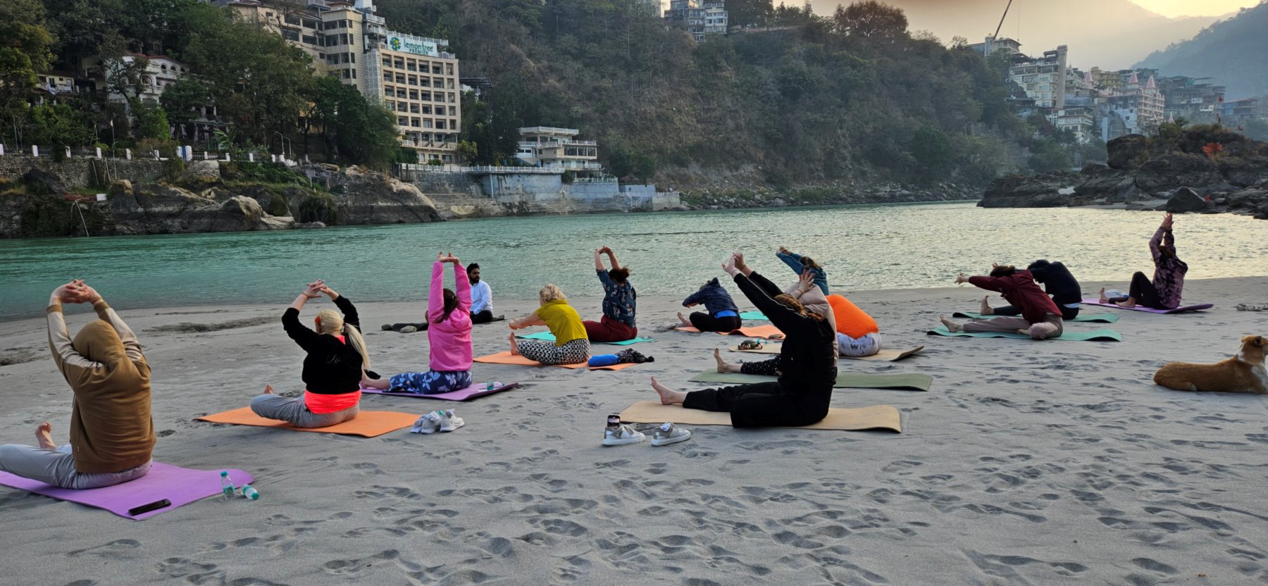 A group stretching at sunrise on a sandy riverbank of the Ganga in Rishikesh